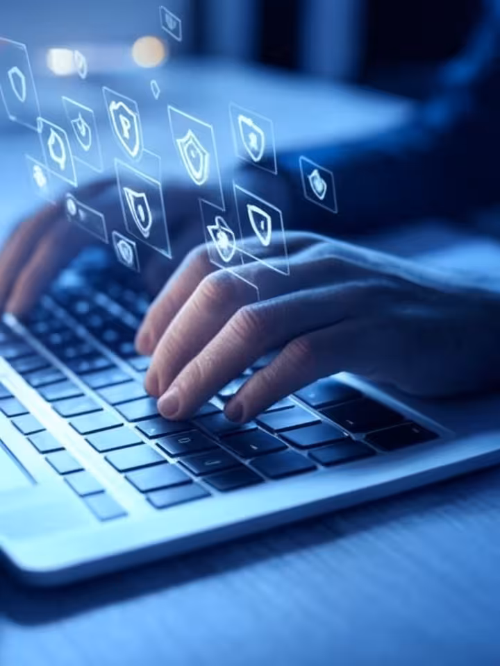 Hands typing on laptop keyboard with warning symbols and shield icons floating above, digital securi